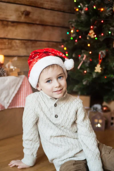 Menino em um chapéu de Natal na frente da árvore decorada — Fotografia de Stock