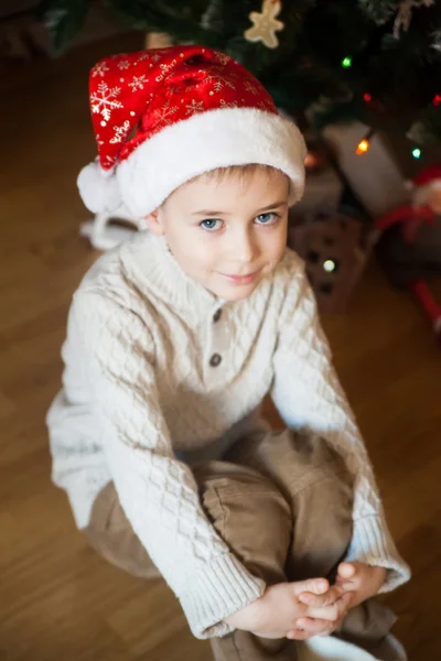 Boy in a Christmas hat in front of decorated tree — Stock Photo, Image