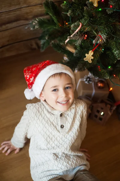 Мальчик в рождественской шляпе перед украшенной елкой — стоковое фото
