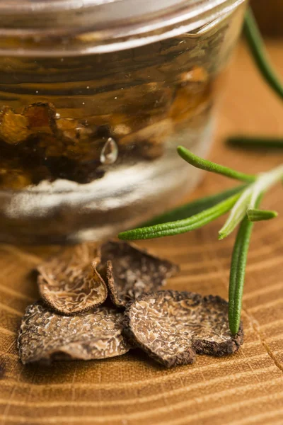 Trufa negra en rodajas en aceite de oliva en frasco pequeño y romero fresco — Foto de Stock