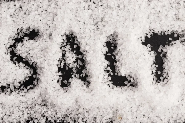 Слово сіль, записане в купі білої гранульованої солі — стокове фото