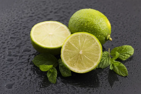 Green limes with mint and water drops on black background — Stock Photo, Image