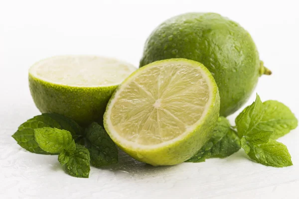 Limas verdes com gotas de hortelã e água sobre fundo branco — Fotografia de Stock