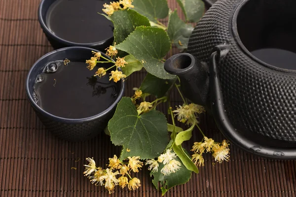 Teiera e tazza con tiglio tè e fiori — Foto Stock