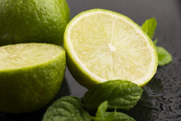 Green limes with mint and water drops on black background — Stock Photo, Image