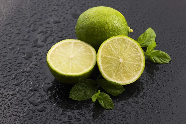 Zielone limonki z miętą i woda spada na czarnym tle — Zdjęcie stockowe