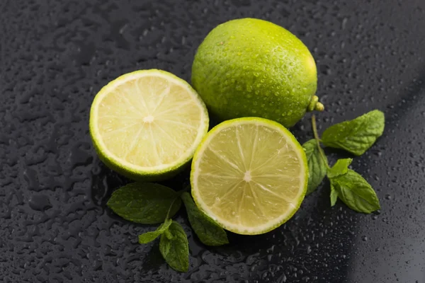 Zielone limonki z miętą i woda spada na czarnym tle — Zdjęcie stockowe