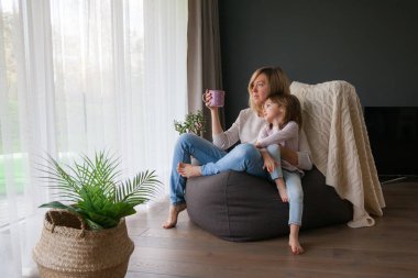 Anne ve küçük kızı evdeki fasulye çuvalında otururken camdan sarılıp bakıyorlar.