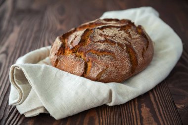 Yakın plan fırınlanmış çavdar ekmeği ahşap bir arka planda keten kumaş içinde daire şeklinde.