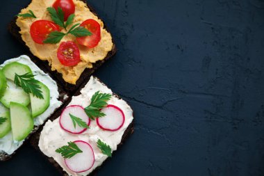 Saf peynir, humus, avokado, turp ve domatesli sağlıklı vejetaryen çavdar ekmekli sandviç. Siyah arkaplan, kopyalama alanı, üst görünüm