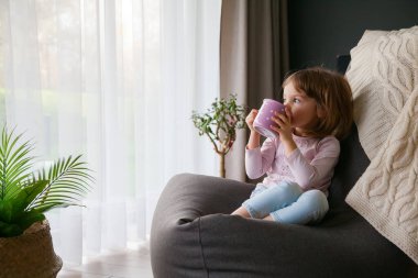 Küçük tatlı bebek rahatlıyor ve bir fincan çay içiyor. Sıcak fasulye koltukta oturuyor.
