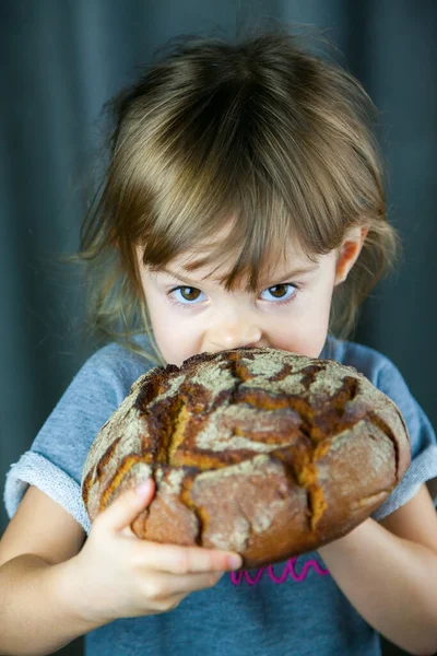 小さな女の子の肖像大きなカリカリ円ライ麦パンを食べて 彼女は非常に空腹 — ストック写真