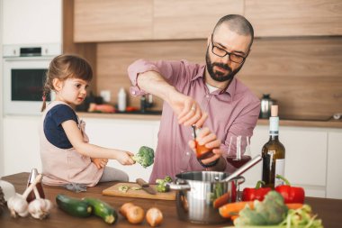 Yakışıklı adam ve küçük tatlı kızı mutfakta birlikte sebze güveci pişiriyorlar. Sağlıklı ve vejetaryen gıda konsepti.
