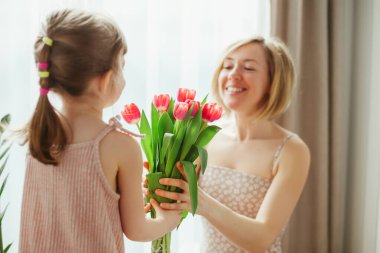 Küçük kız annesini tebrik ediyor ve ona çiçek veriyor. Anneler Günün kutlu olsun! Anne ve kızı gülümsüyor ve birlikte vakit geçiriyorlar. Lalelere odaklan..