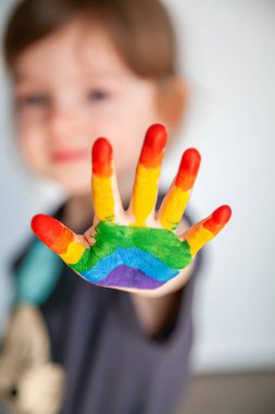 Üzerinde gökkuşağı resmi olan küçük şirin bir kız elini gösteriyor.