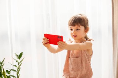 Cep telefonu olan şirin küçük bir kız. Akıllı telefonuyla selfie çekiyordu. Dijital nesil ve telefon bağımlılığı kavramı.