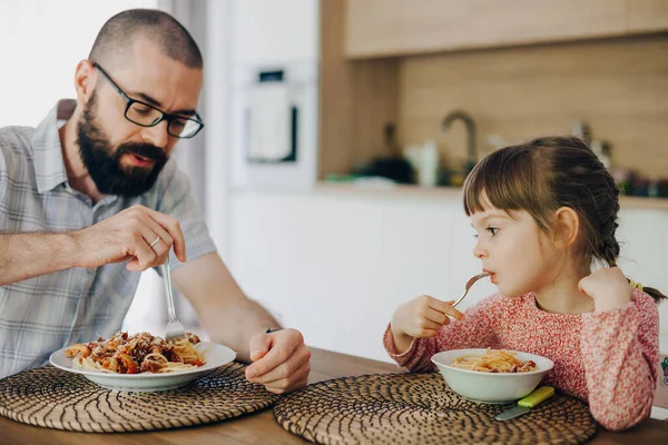 一个留着胡子的男人和他可爱的小女儿坐在厨房里吃着意大利面和酱汁 — 图库照片