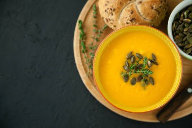 Yakın plan vejetaryen ev yapımı balkabağı çorbası. Tohumlar, otlar ve çörekler, siyah arka planda.