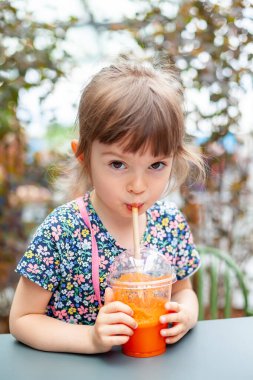 Tatlı küçük kız dışarıda saman içerek taze havuç suyu içiyor.