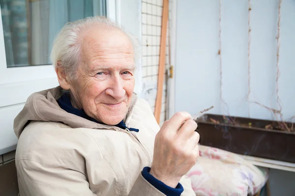 Usmívající se starý muž držící cigaretu — Stock fotografie