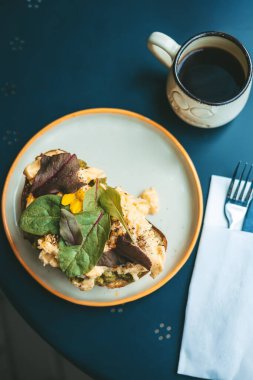 Lezzetli bir kafe brunch 'ının tepesinde gurme avokado tostu, çırpılmış yumurta, taze yeşillikler ve koyu desenli bir masada bir kupa kahve, sağlıklı yemek ve menü kavramları için mükemmel.