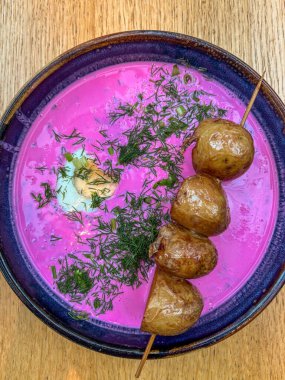 Canlı pembe Litvanya soğuk borş çorbası ya da saltibarsciai koyu mavi bir kasede, dereotlu haşlanmış yumurta ve şişte kızarmış patates ile servis edilir.