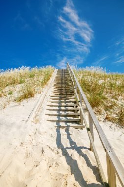 Litvanya 'daki Curonian Spit' in kum tepesine çıkan ahşap merdivenler kıyı seyahati veya doğa koruma kavramı için parlak mavi bir gökyüzünün altında