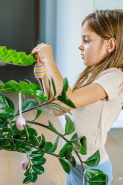 Çocuk elleri zamioculcas üzerine dekoratif yumurtalar asıyor oturma odasındaki bitki dalları yaratıcı paskalya geleneğini ve yerel etkinlikleri temsil ediyor.