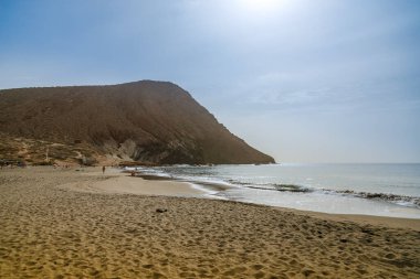Kanarya adalarındaki doğal bir kıyı rezervinin panoramik görüntüsünde kırmızı volkanik koni ve Atlantik okyanus dalgaları yaz seyahatleri rehberleri veya ekolojik turizm web siteleri için kullanılır.