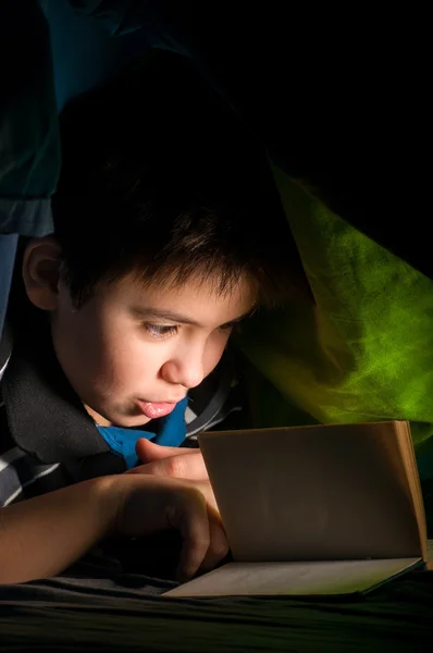 Pojke läser en bok under täcket — Stockfoto