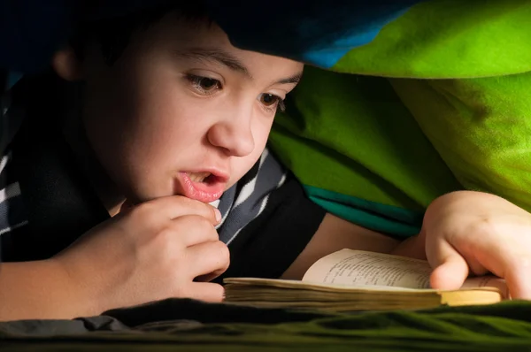 Chico leyendo un libro bajo las cubiertas — Foto de Stock