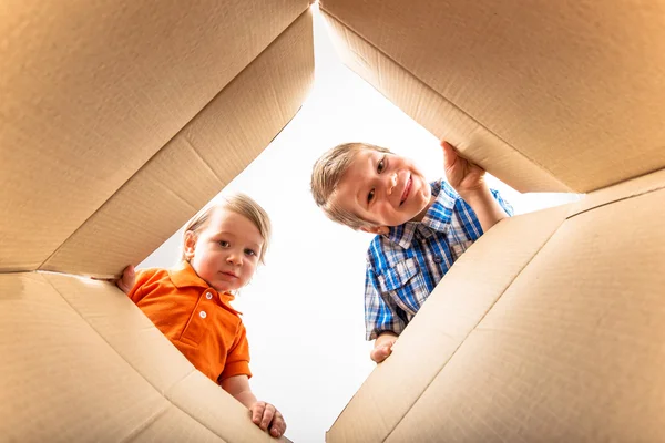 Due ragazzini che aprono una scatola di cartone e guardano dentro con sorpresa . — Foto Stock
