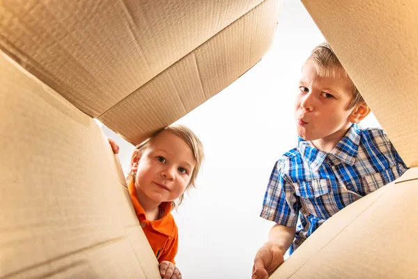 Dos niños pequeños abriendo la caja de cartón y mirando dentro con sorpresa . —  Fotos de Stock