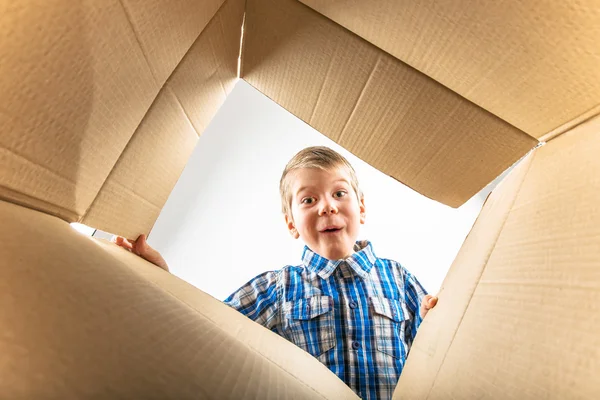 Niño abriendo caja de cartón y mirando dentro con sorpresa —  Fotos de Stock