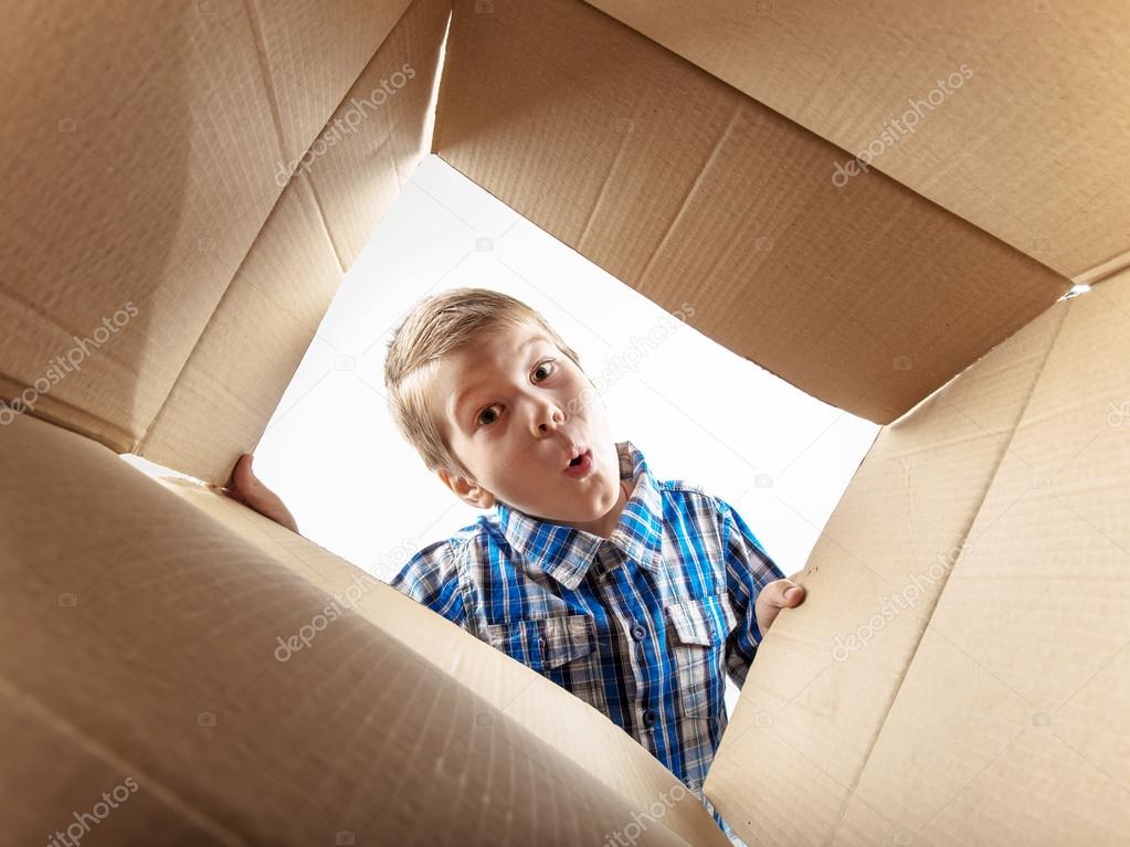 Child opening cardboard box and looking inside with surprise