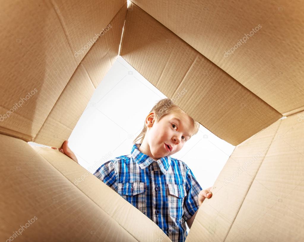 Child opening cardboard box and looking inside with surprise