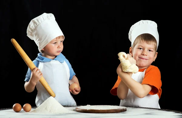 Два маленьких хлопчика роблять піцу або тісто для макаронних виробів. Ізольовані на чорному — стокове фото