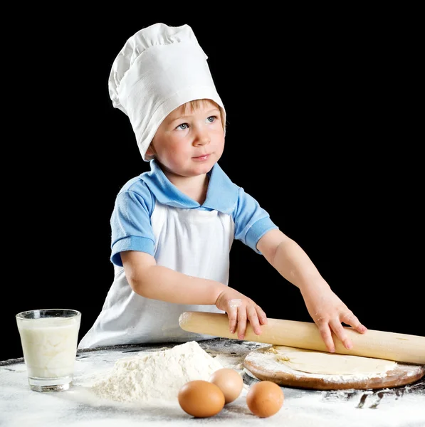 Маленький хлопчик робить піцу або тісто для макаронів. Ізольовані на чорному — стокове фото
