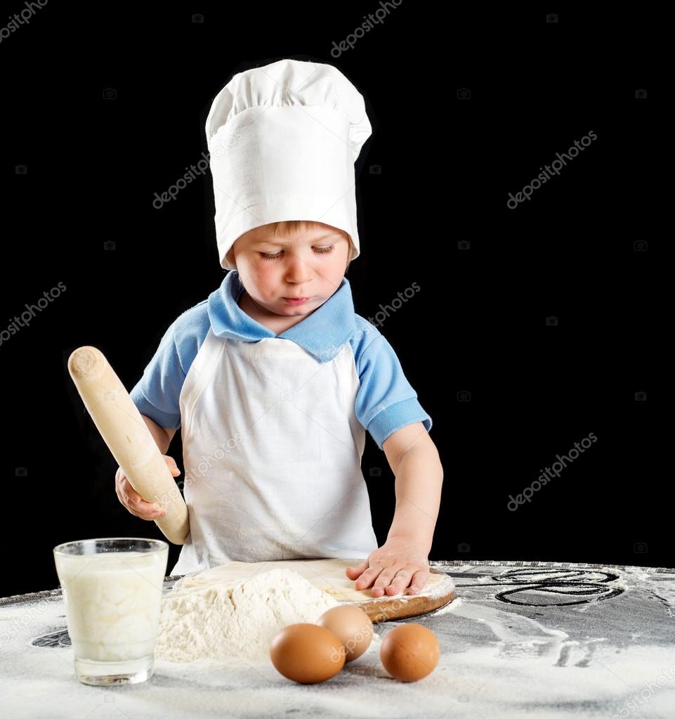 Little boy making pizza or pasta dough. Isolated on black