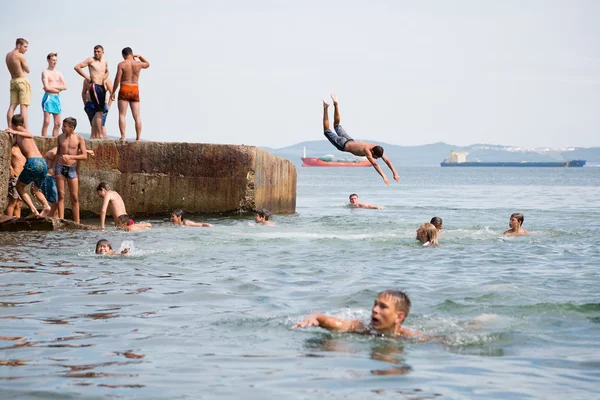 Joyful children jumping and diving into the sea from old dock — Stock Photo, Image