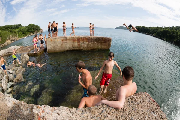 Fröhliche Kinder springen und tauchen vom alten Dock ins Meer — Stockfoto