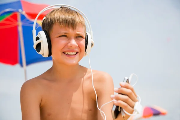 Menino com fones de ouvido usando um smartphone na praia — Fotografia de Stock