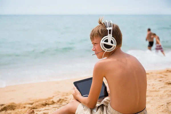 Niño jugando tableta de ordenador sentado junto al mar Fotos De Stock