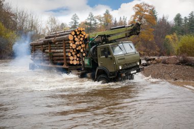 Heavy truck for transportation of logs moves ford in the river clipart