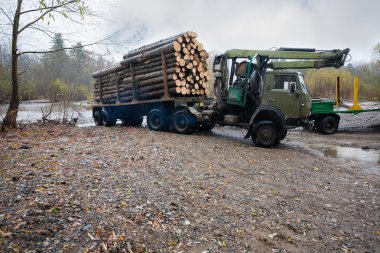 Heavy truck for transportation of logs standing on the bank of r clipart