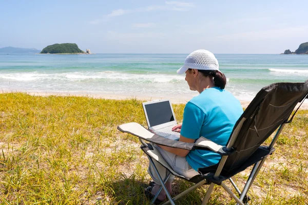 Middle-aged woman uses a laptop while on the beach — Stock Photo, Image