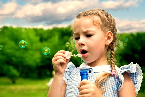 Flicka blåser såpbubblor i sommaren park — Stockfoto