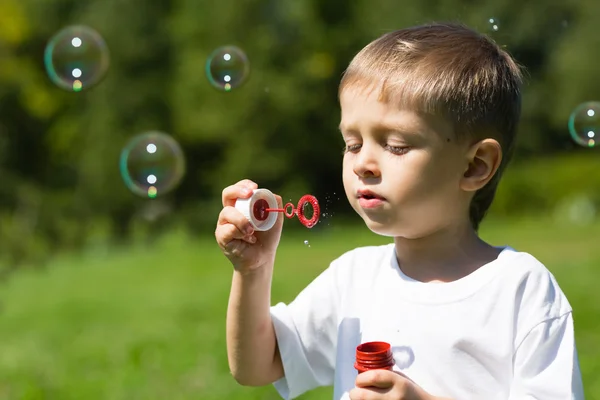 Mignon garçon souffler savon bulles dans un parc — Photo