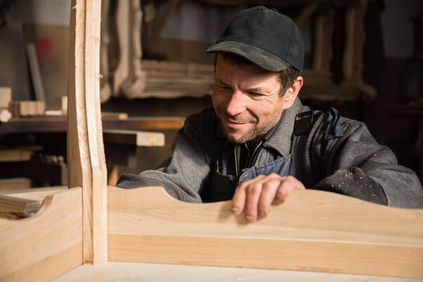 Smiling carpenter examines produces furniture 