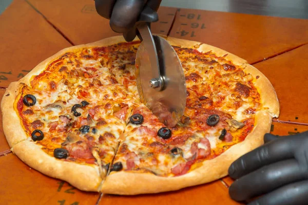 Cutting pizza with a round cutter knife. Close-up of delicious pizza being cut into pieces.